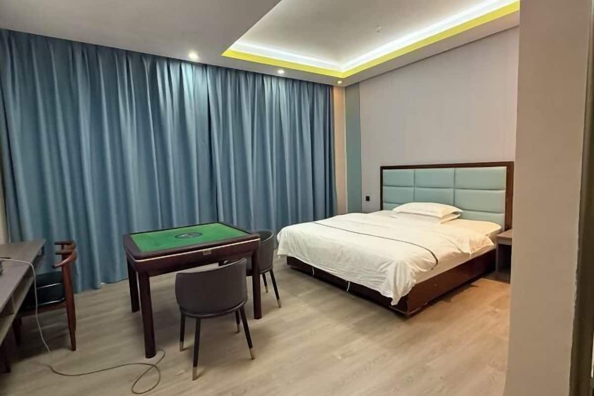 A hotel room with a bed, a desk with a green felt table, and a chair.