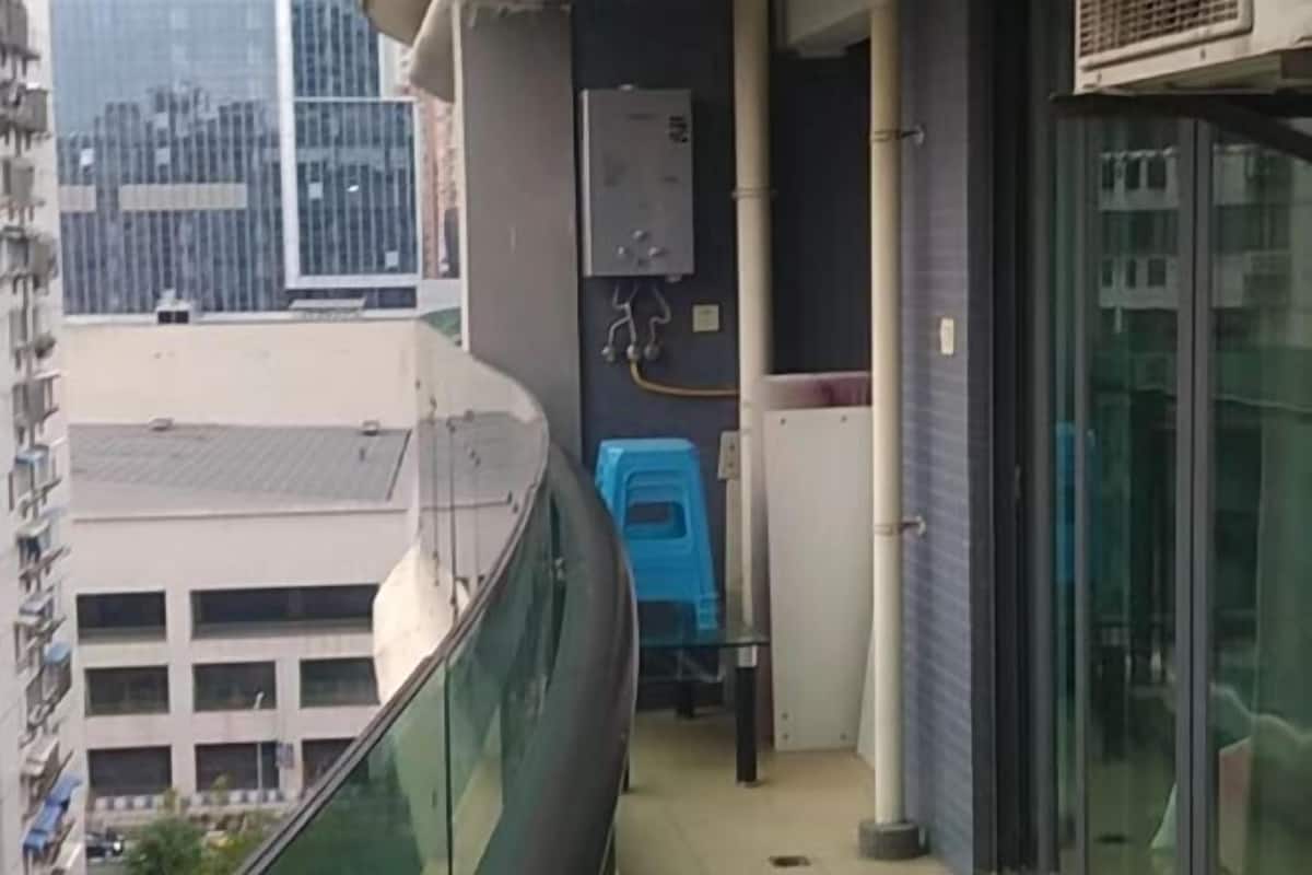 Un pasillo estrecho con barandilla de vidrio, una silla de plástico azul y un cuadro eléctrico.