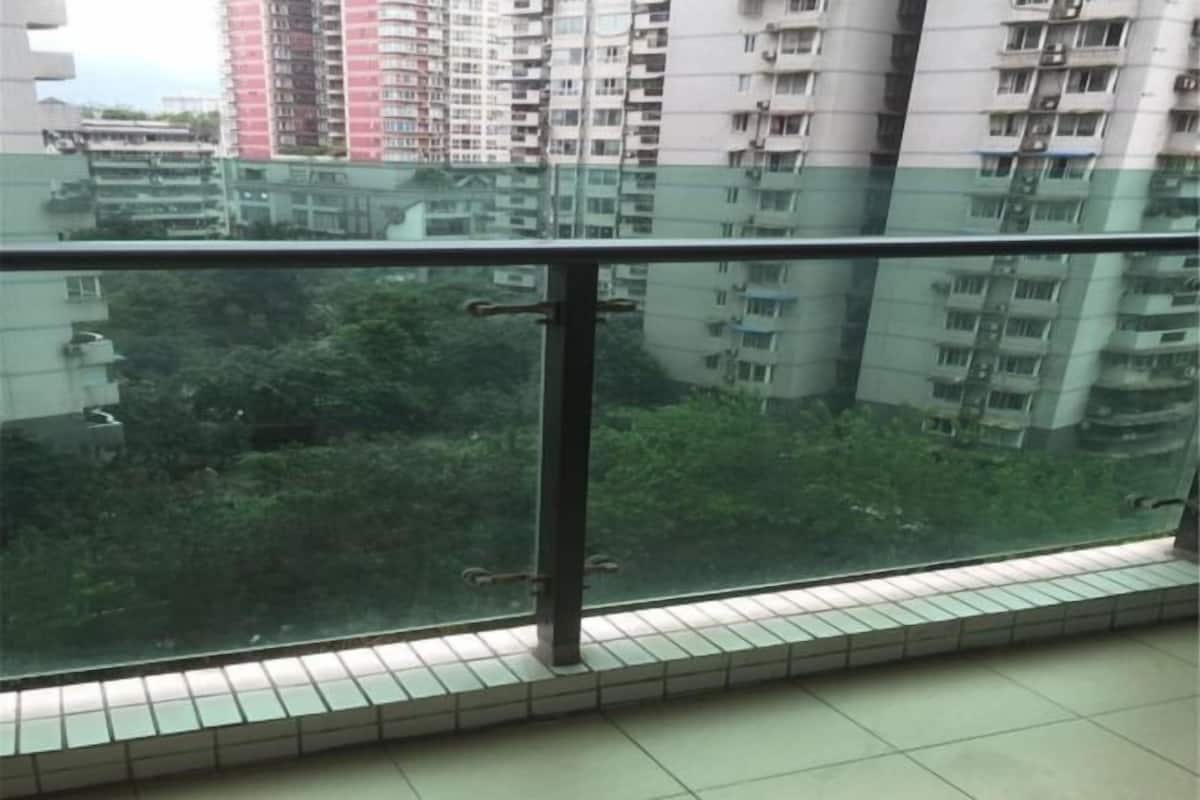 Un balcón con barandilla de vidrio que da a una zona residencial con varios edificios altos.