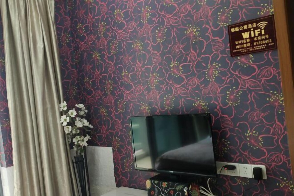 A room with a patterned wallpaper, a flat-screen TV, a power outlet, and a flower vase.