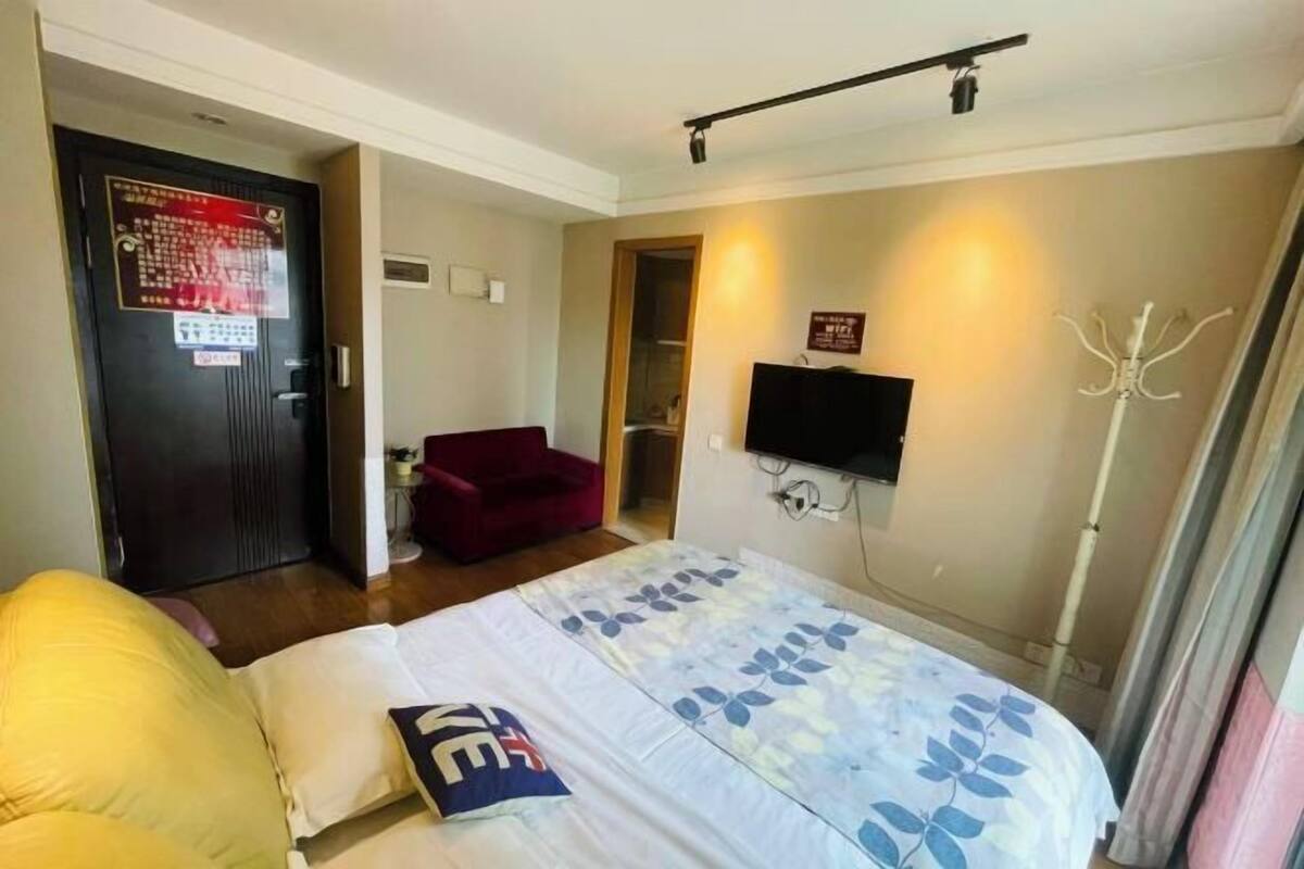 Habitación de hotel con cama, una silla roja, televisor montado en la pared y una puerta con un letrero.
