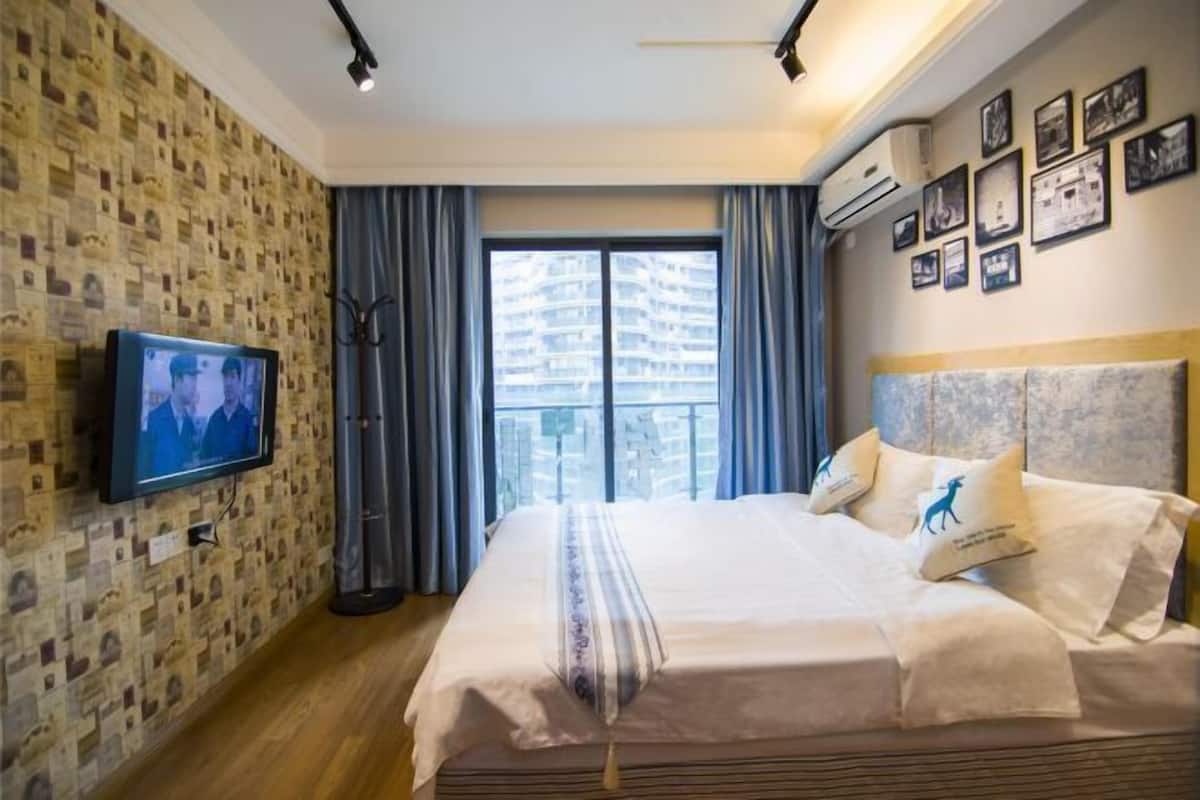 Habitación de hotel con una cama grande, un televisor en la pared, un balcón con cortinas y un papel tapiz estampado.