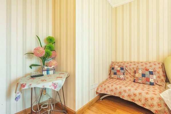 A room with a striped wallpaper, a floral sofa with patterned cushions, a small table with a floral tablecloth, and a vase with flowers. - Jinlin Hotel (Chongqing)