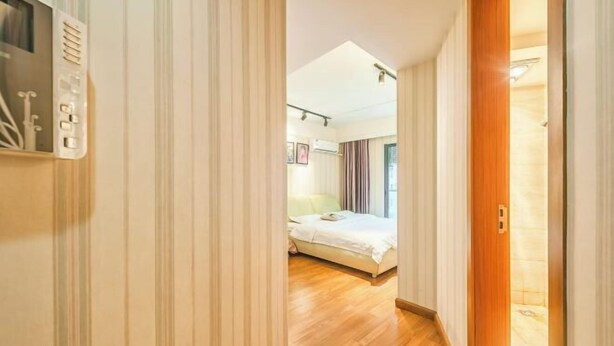 Ein Flur, der zu einem Schlafzimmer mit Bett, Holzboden und weißer Tür führt.