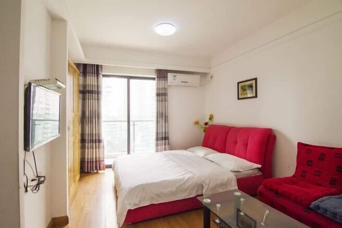 Una habitación de hotel con una cama, un sofá rojo, un televisor y un equipo de aire acondicionado.