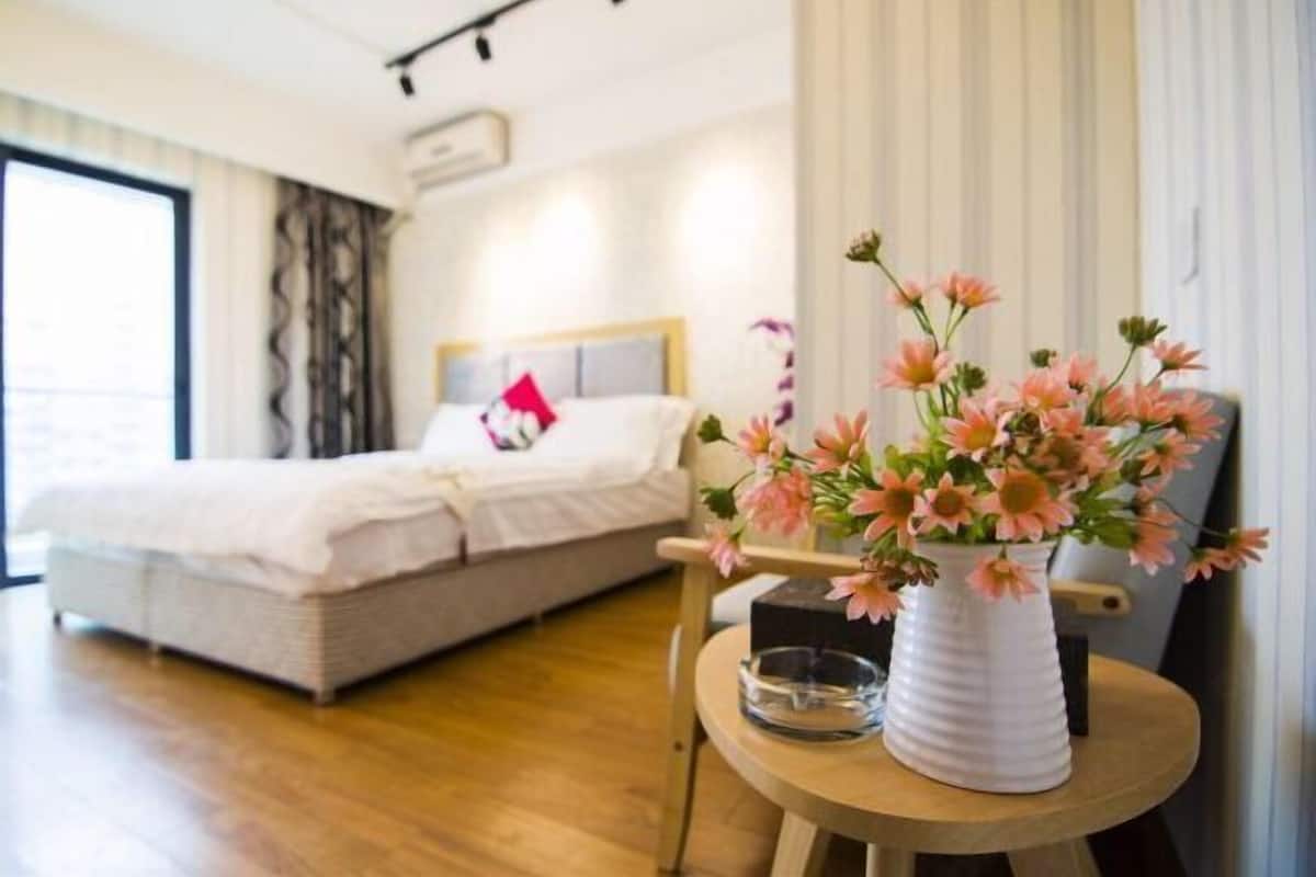 Habitación de hotel con una cama, una mesa redonda de madera con un florero y vistas de la ciudad a través de amplios ventanales.
