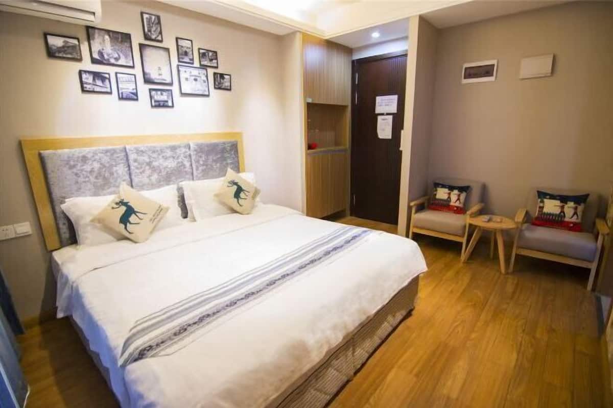 Habitación de hotel con una cama grande, cabecera de madera, una pequeña zona de estar con dos sillones y una pared decorada con cuadros.