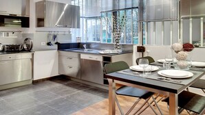 A modern kitchen with stainless steel appliances, a dining table set for four, and a view of the outdoors through large windows. - A PARISIAN LOFT LOCATED JUST FEW MINUTES FROM RUE MONTORGUEIL (Paris)