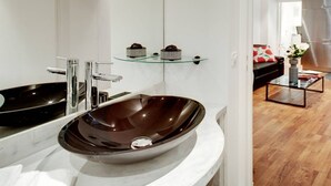A modern bathroom with a large, dark, oval-shaped vessel sink, a chrome faucet, and a glass shelf above the mirror. - A PARISIAN LOFT LOCATED JUST FEW MINUTES FROM RUE MONTORGUEIL (Paris)