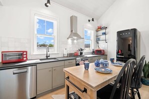 A modern kitchen with stainless steel appliances, a wooden dining table, and a view of the outdoors.