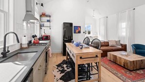 A modern kitchen with a central island, a dining area with a wooden table, a sofa, and a coffee table. - Casa Romeo | Gorgeous Ybor Apt, Steps to 7th Ave (Tampa)