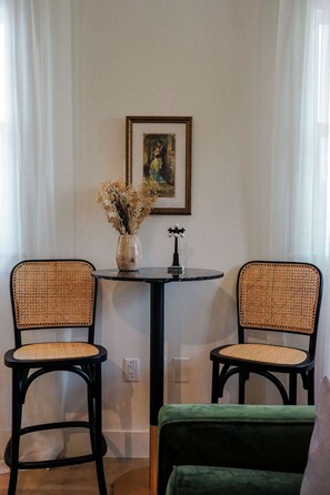 Una habitación con dos sillones de mimbre, una mesita redonda con un jarrón de flores secas y un cuadro enmarcado en la pared.