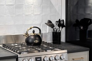 Una cocina con estufa a gas, hervidor y un recipiente para utensilios.