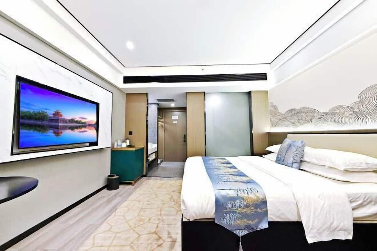 Una habitación de hotel moderna con un televisor de pantalla plana grande montado en la pared, una cama con colcha azul y blanca, y un mural decorativo.