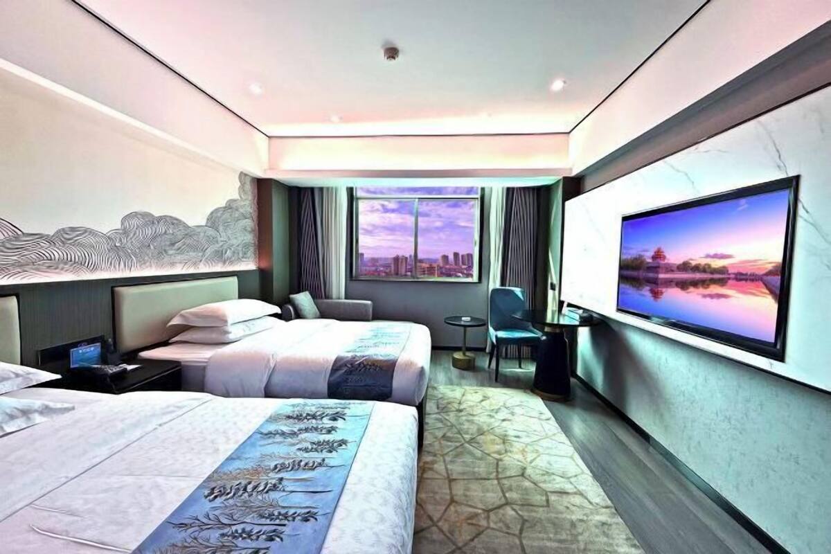 Habitación de hotel con dos camas, televisión, escritorio y vista a la ciudad.