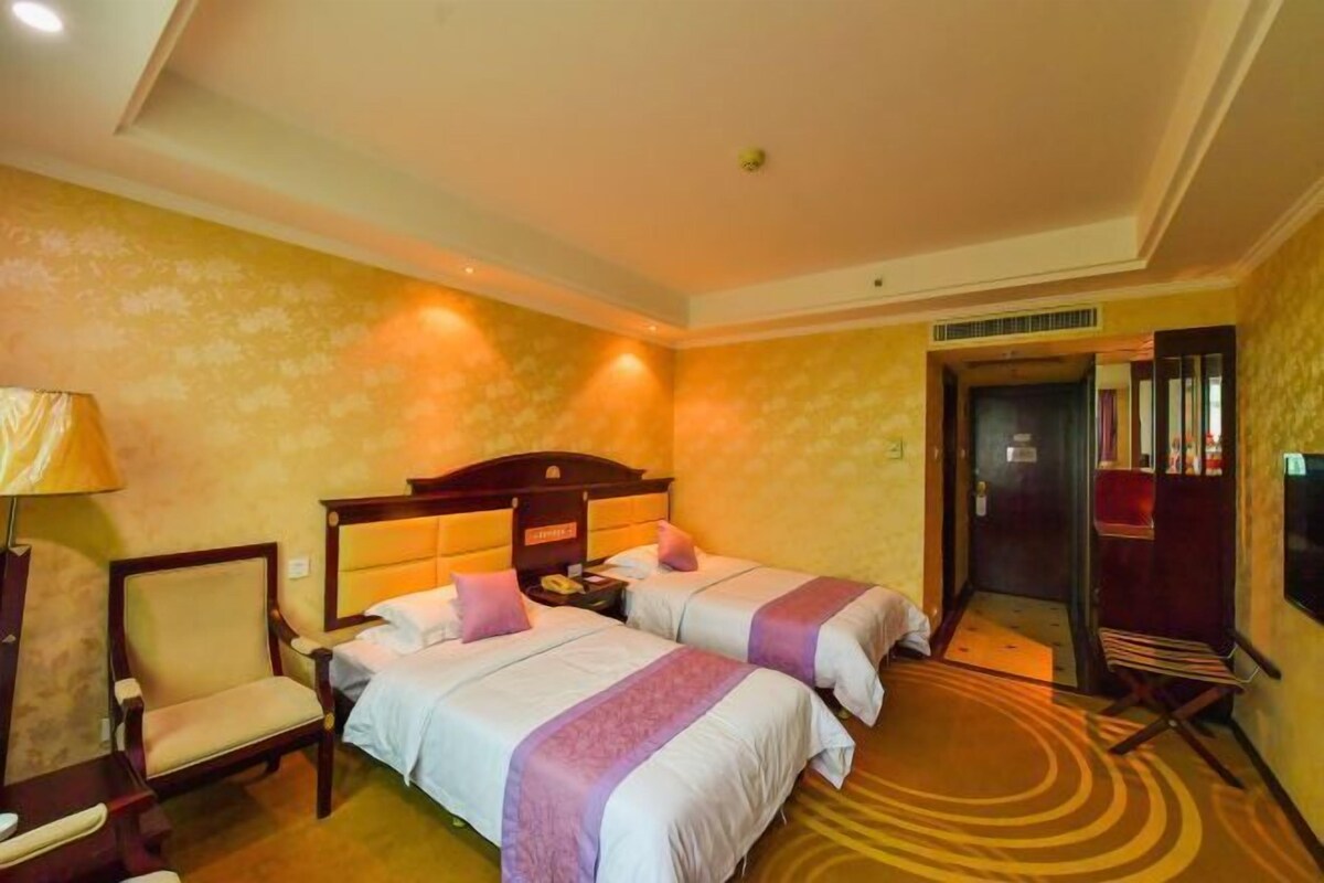Une chambre d’hôtel avec deux lits, une chaise, une table de chevet et une porte donnant sur un couloir.