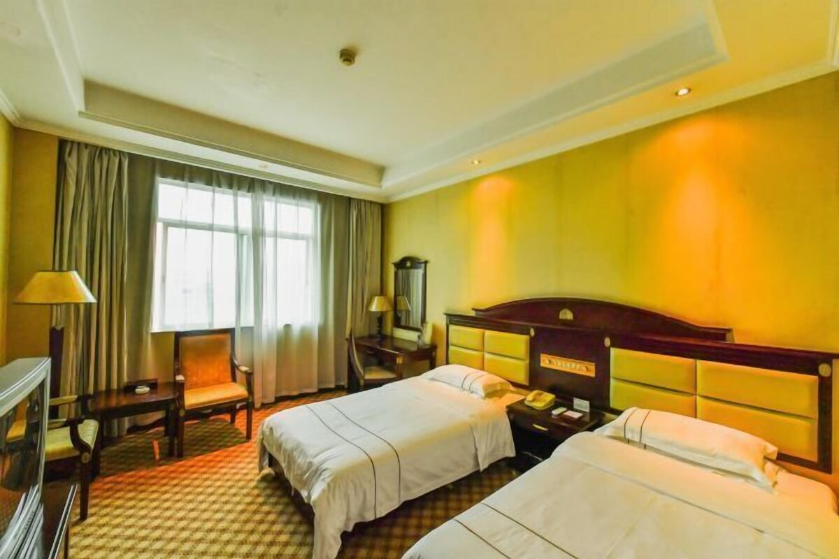 Une chambre d’hôtel avec deux lits, un bureau, une chaise, une télévision et une fenêtre avec des rideaux.