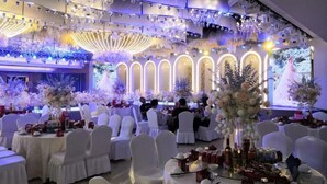 Una sala de banquetes amb taules rodones, cadires blanques i centrals florals.