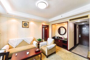 Un salon comprenant un canapé, un fauteuil et une table basse. Il y a un miroir au mur, une porte donnant sur une autre pièce et une petite table sur laquelle sont posés divers objets.