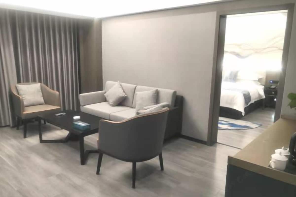 Una habitación de hotel moderna con sofá, sillón, mesa de centro y escritorio con lámpara.