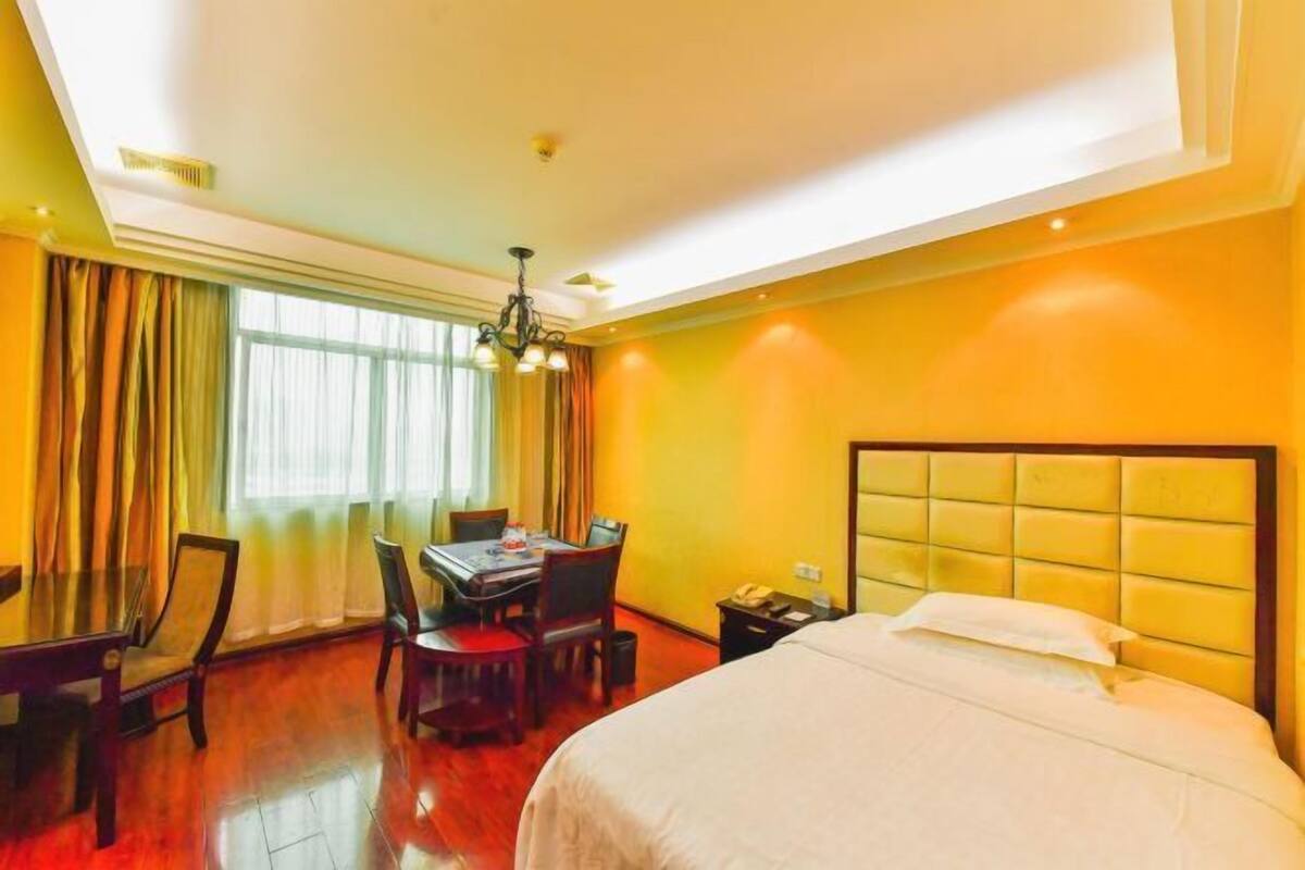 Habitación de hotel con cama, mesa de comedor, sillas, candelabro y ventana con cortinas.