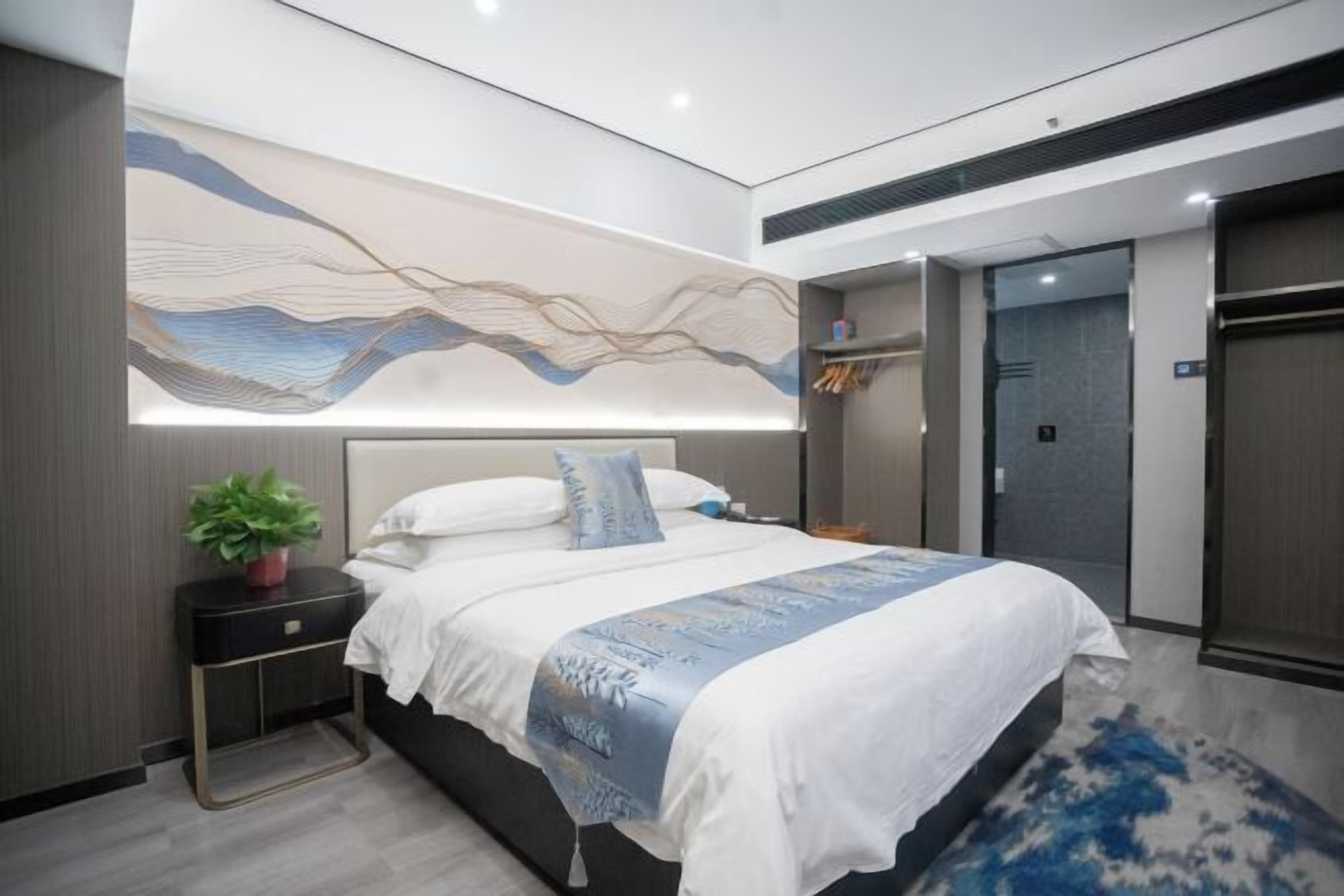 Habitación de hotel moderna con una cama grande, una mesita de noche con una planta y una obra de arte colgada en la pared.