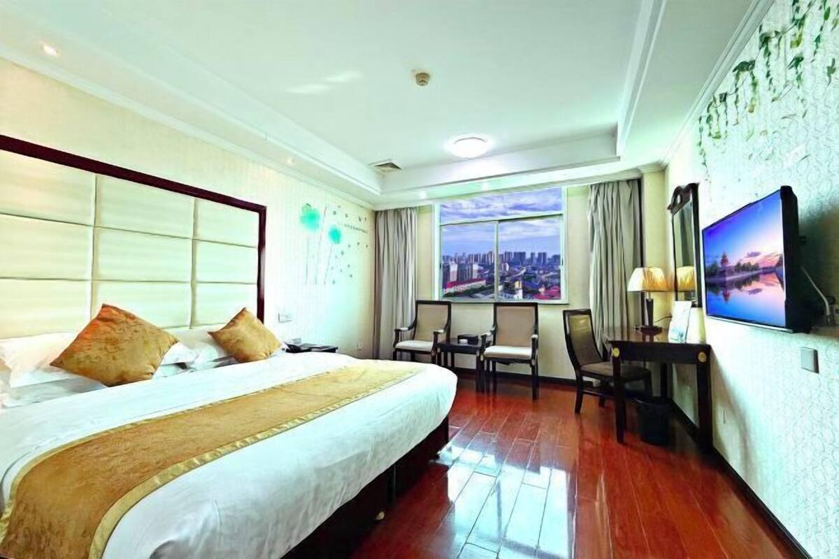 Habitación de hotel con una cama grande, televisión, escritorio con sillas y vistas a un paisaje urbano por la ventana.