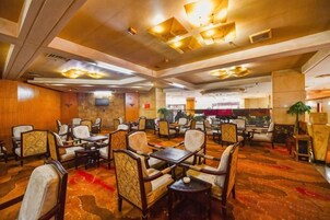 Un comedor de hotel con varias mesas y sillas, una alfombra estampada e iluminación empotrada en el techo.