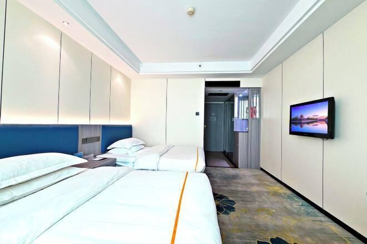 Habitación de hotel con dos camas, un televisor en la pared y una puerta que da al baño.