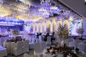 A banquet hall with round tables, white chairs, and floral centerpieces.