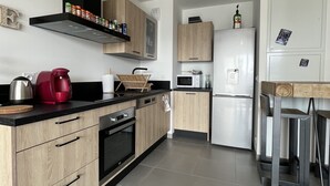 A modern kitchen with wooden cabinets, a stainless steel range hood, a red coffee maker, and a white refrigerator. - Appart-Hotel - The sunbath (Annecy)