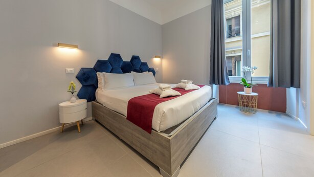 Et moderne hotelværelse med en stor seng, et natbord med blomster og udsigt til balkonen.