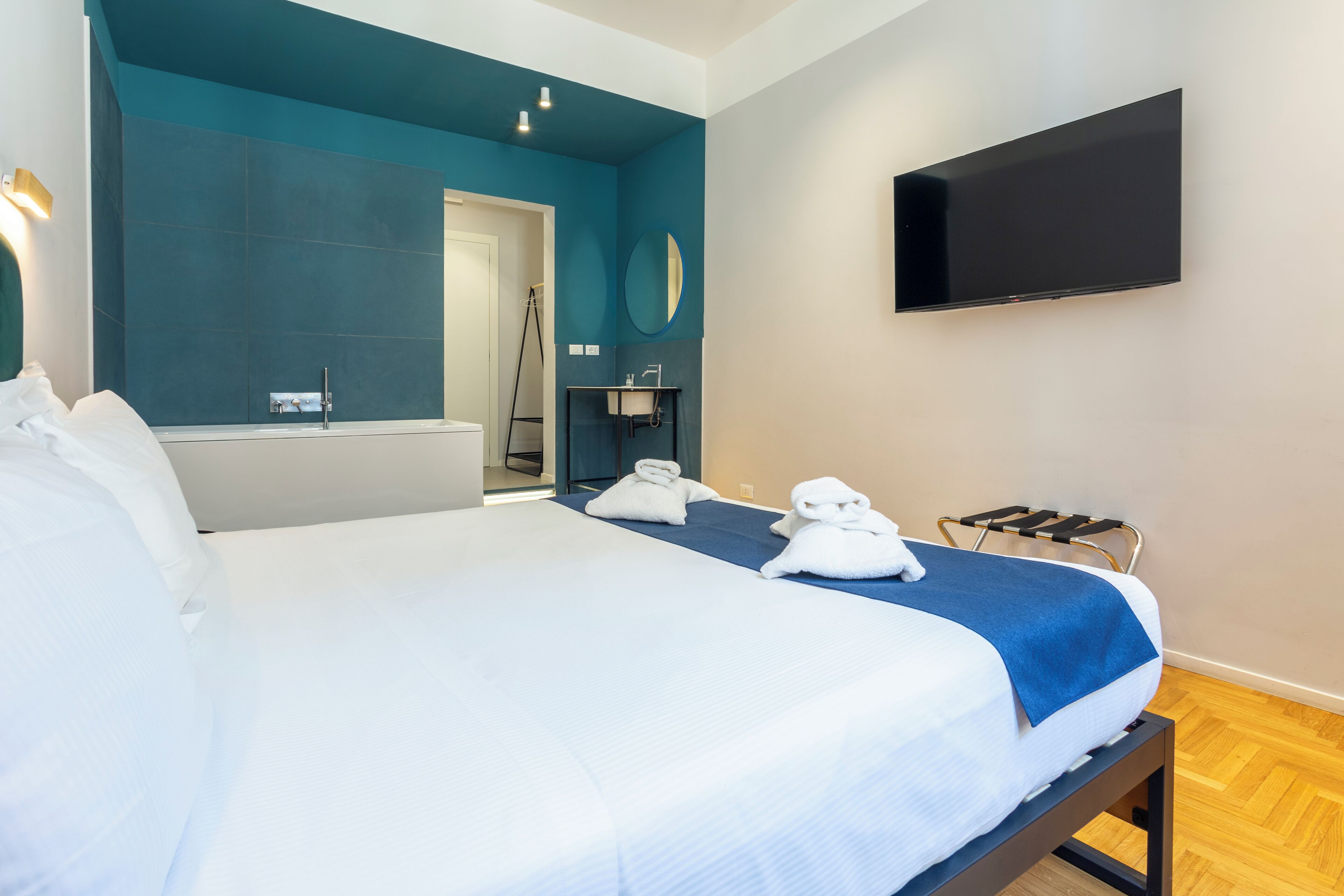 Une chambre d’hôtel avec un grand lit, un téléviseur fixé au mur et une salle de bain visible à travers une porte ouverte.