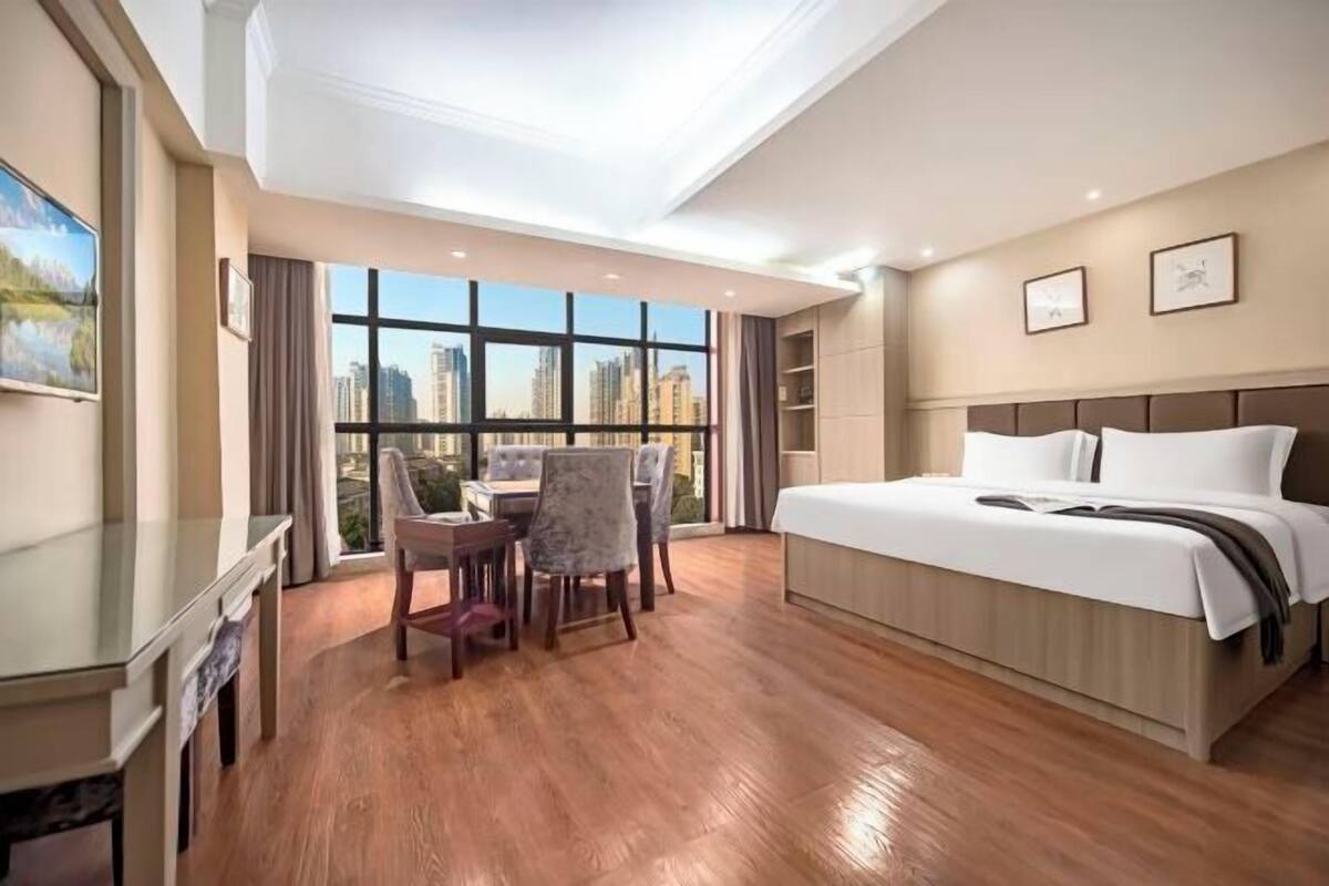 A hotel room with a large bed, a desk, and a dining area with chairs.