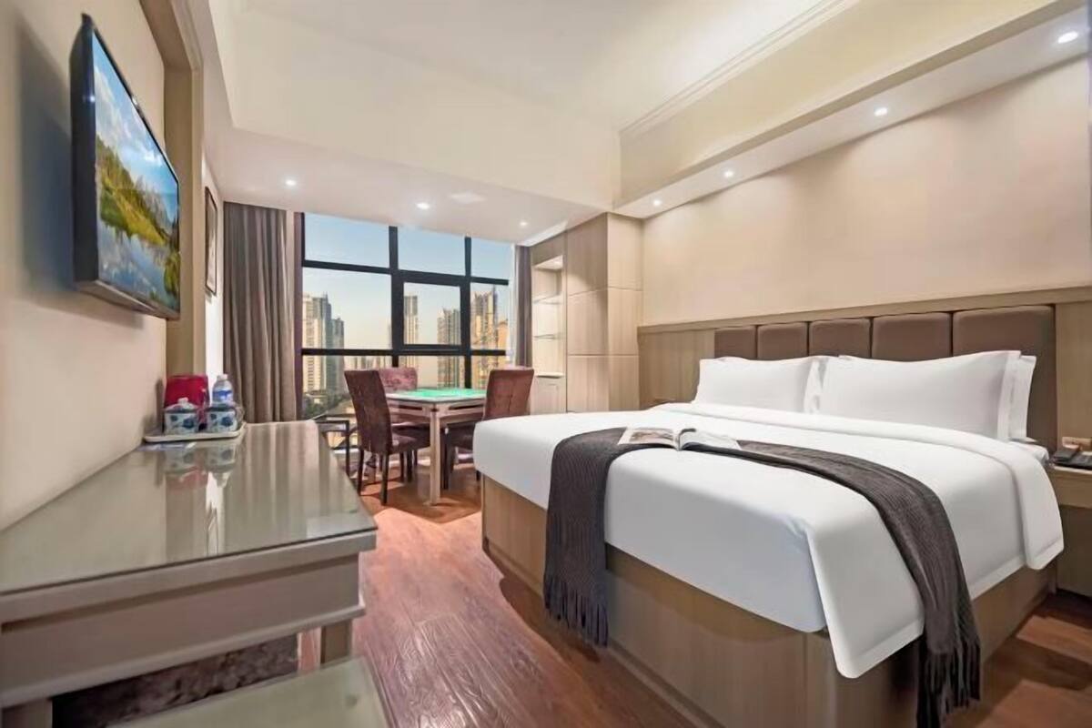 A hotel room with a large bed, a desk, and a view of the city skyline.