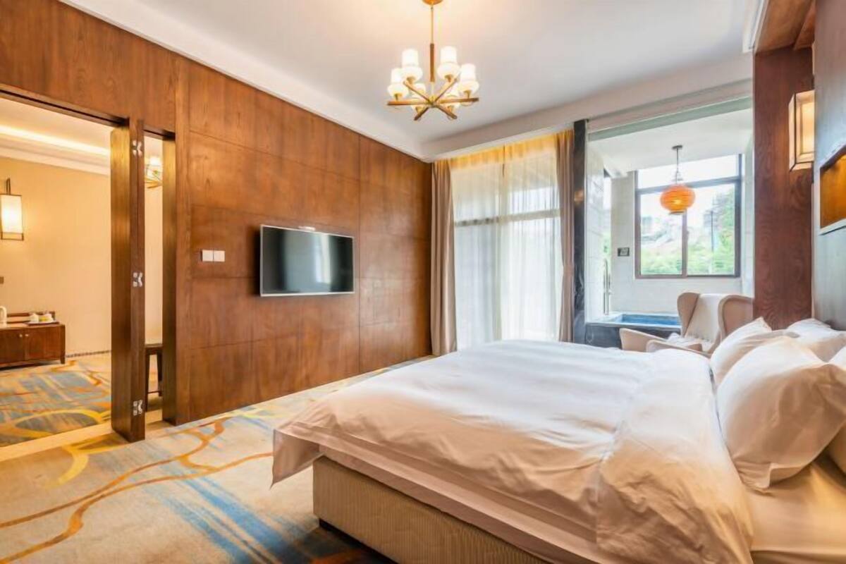 Ein Hotelzimmer mit einem großen Bett, einem flachbildfernseher an der Wand und einer Chandelüster.