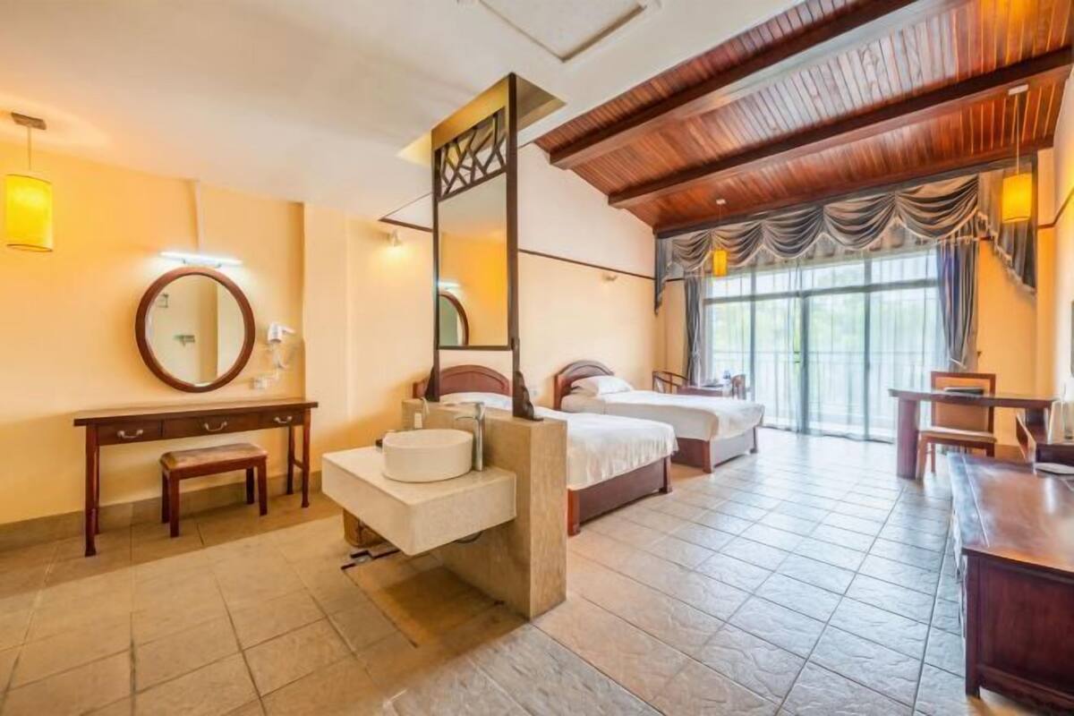 Ein Hotelzimmer mit Holzboden, einem großen Spiegel, einem runden Waschbecken, zwei Betten und einem großen Fenster.