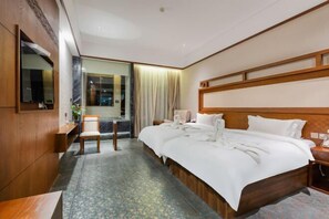Habitación de hotel con una cama grande, un escritorio, una silla, un televisor y una ventana con cortinas.