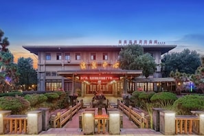 Et hotel med traditionel arkitektur, en central indgang og et velholdt udendørs område med siddepladser.