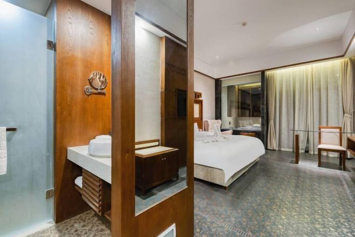 Ein Hotelzimmer mit einem Holznähtisch, einem Bett, einem großen Spiegel und Blick auf die Stadt durch das Fenster.