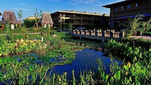 Un hotel con piscina rodeado de nenúfares y plantas tropicales, con un puente que conecta diferentes áreas.