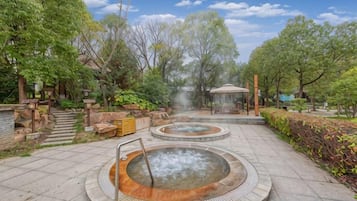 A hot spring area with stone steps leading to a gazebo, surrounded by trees and greenery.