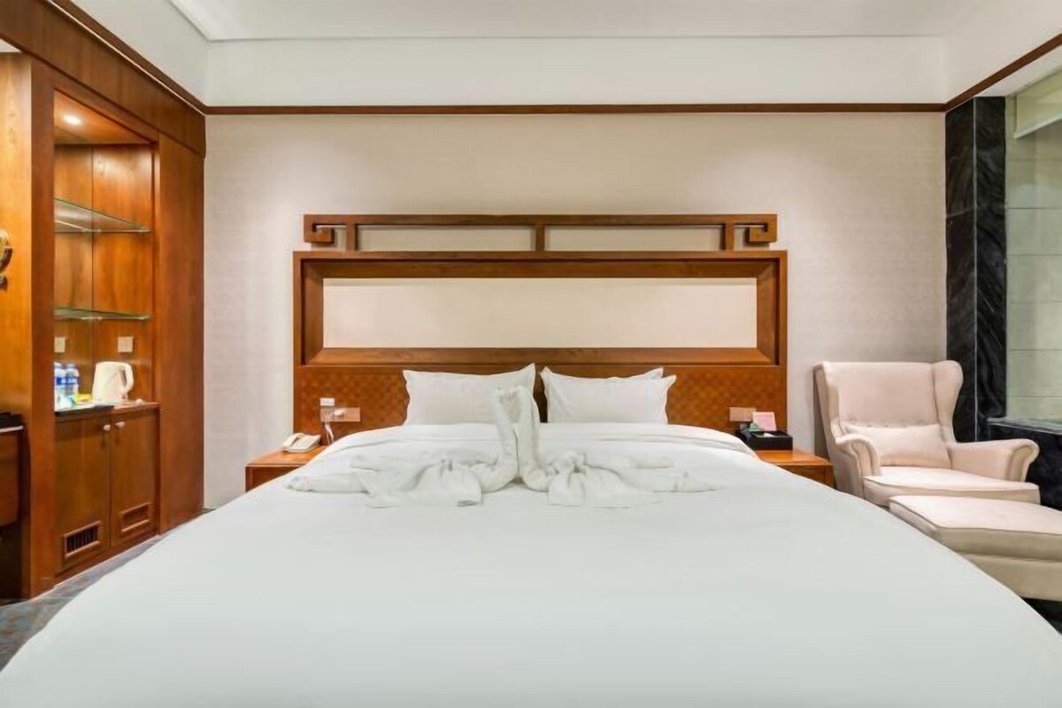 Habitación de hotel con una cama grande, cabecero de madera, dos mesitas de noche, una silla y un armario.