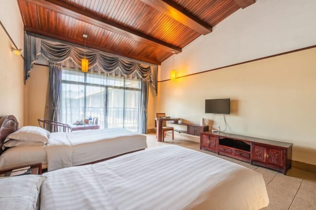 Habitación de hotel con dos camas, un escritorio, televisor y un amplio ventanal con cortinas.