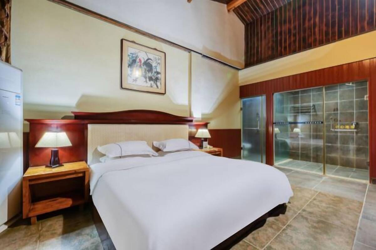 Ein Hotelzimmer mit einem Bett, Nachttischen, einer Lampe, einem gerahmten Bild an der Wand und einer Schiebetür zu einem Badezimmer.