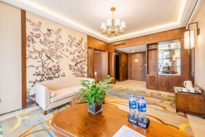 Un hall de hotel con un sofá, una mesa de centro de madera con una planta y botellas de agua, una araña y una alfombra estampada.
