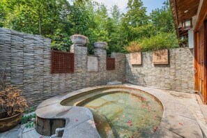 Un patio de paredes de piedra con una piscina circular, plantas en macetas y una puerta de madera.