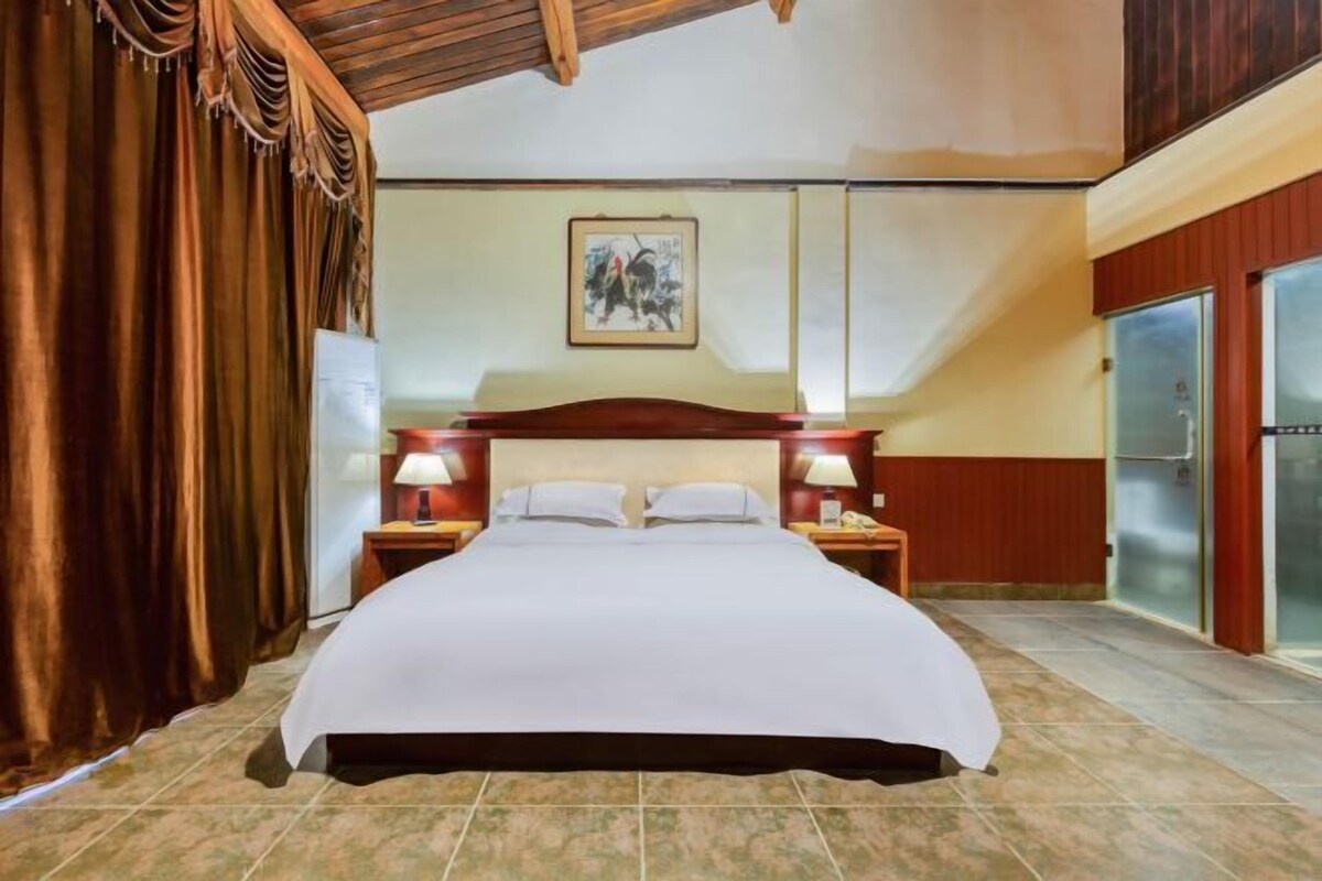 Habitación de hotel con una cama grande, dos mesitas de noche con lámparas, una obra de arte en la pared, un refrigerador y un techo de madera.