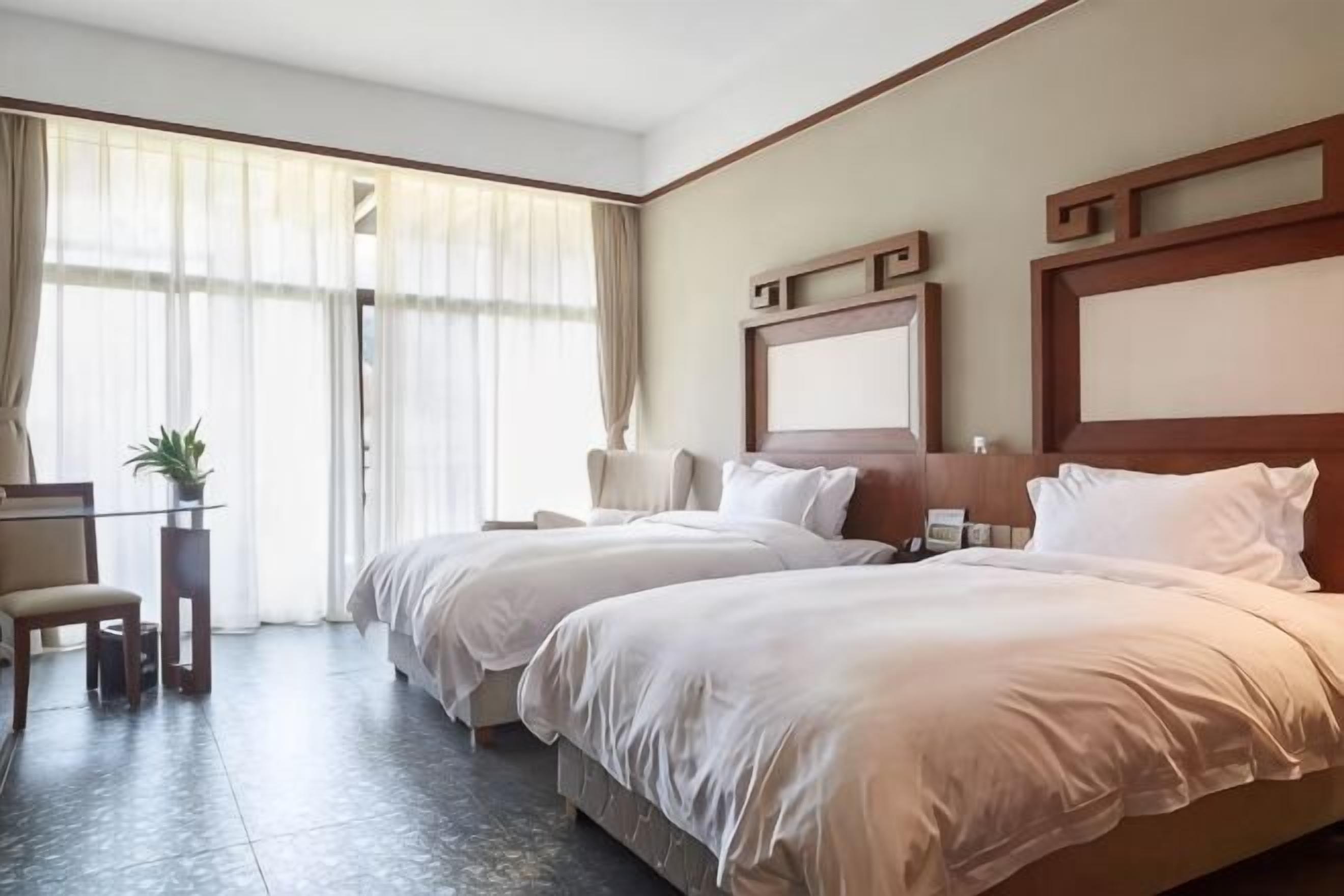 Una habitación de hotel con dos camas, un escritorio, una silla y un ventanal con cortinas.