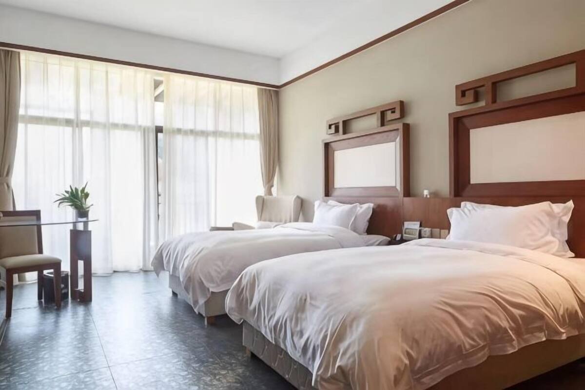 Ein Hotelzimmer mit zwei Betten, einem Schreibtisch, einem Stuhl und einem großen Fenster mit Vorhängen.